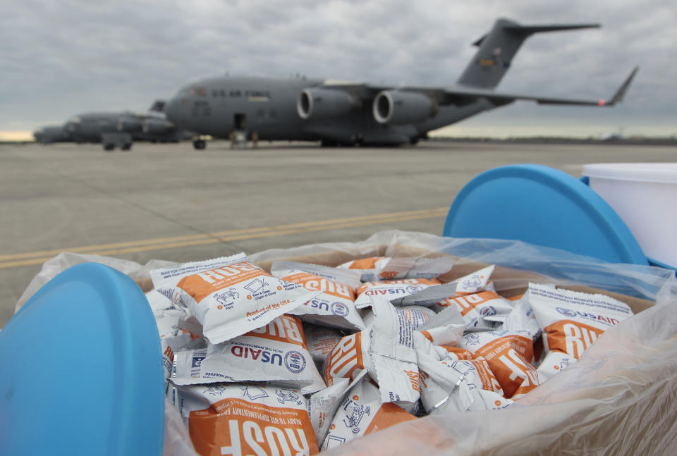 Un contenedor con varias bolsas de suplementos alimentarios se observa cerca de un avión de carga C-17 que transportan ayuda humanitaria, el sábado 16 de febrero de 2019, en una base de la Fuerza Aérea de Estados Unidos en Homestead, Florida. (AP Foto/Luis M. Álvarez)