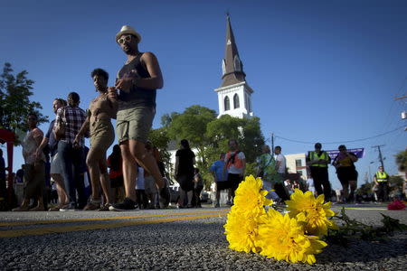 People walk past a bunch of flowers left in memorial on the ground as they take part in a "Black Lives Matter" march past Emanuel African Methodist Episcopal Church in Charleston, June 20, 2015. REUTERS/Carlo Allegri