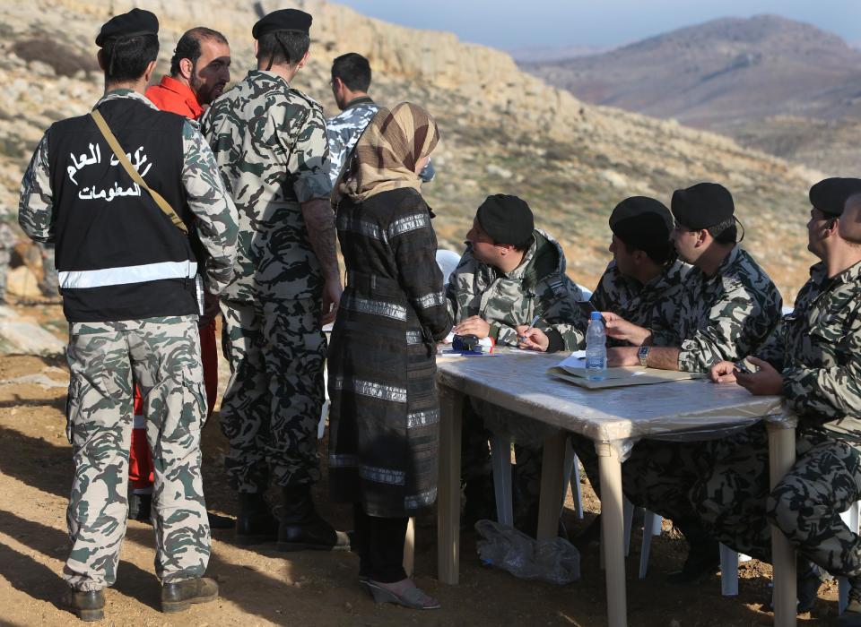 Lebanese General Security forces check the identity card of a Lebanese woman, center, as she leaves the Tfail village, in the Ras al-Haref mountains at the Lebanese-Syrian border, eastern Lebanon, Tuesday April 22, 2014. A Lebanese convoy of soldiers, clerics and Red Cross officials delivered aid Tuesday to a remote village near the Syrian border that was bombed by Syrian government aircraft and blocked by Lebanese militants fighting alongside President Bashar Assad’s forces in the civil war next door. Hezbollah fighters have been patrolling the area on the Lebanese side and fighting has flared up inside Syria, cutting Tfail’s residents off from all sides for months. (AP Photo/Hussein Malla)