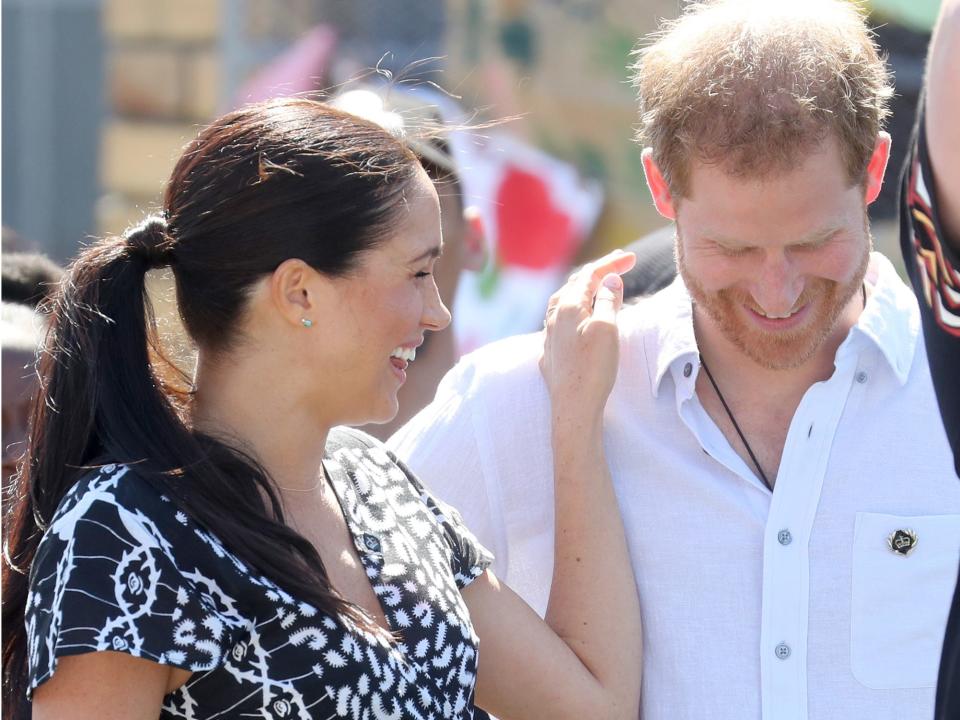 Meghan Markle laughs and places her hand on Prince Harry's shoulder