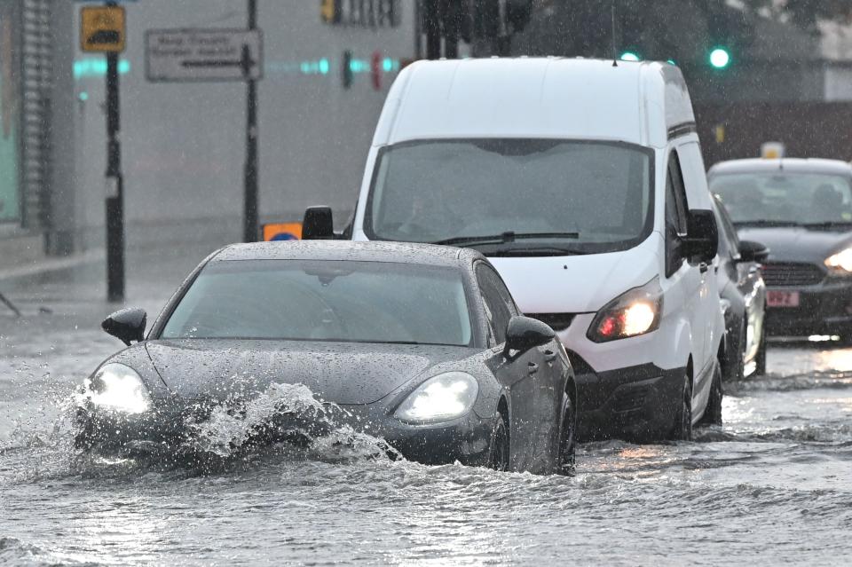 <p>Cars drive through deep water on a flooded road in The Nine Elms district of London on July 25, 2021 during heavy rain. - Buses and cars were left stranded when roads across London flooded on Sunday, as repeated thunderstorms battered the British capital. (Photo by JUSTIN TALLIS / AFP) (Photo by JUSTIN TALLIS/AFP via Getty Images)</p>
