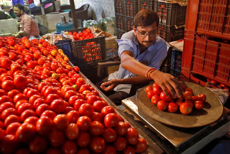 A vendor weights tomatoes for a customer at a vegetable market in Ahmedabad