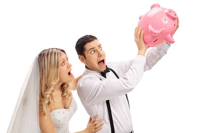 We see a bride and groom, holding an empty piggy bank upside down while looking alarmed, with their mouths open.