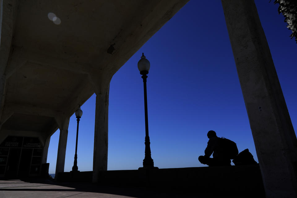 A man finds shade under a bridge connecting the Oceanside pier to Pacific Street Friday, Oct. 15, 2021, in Oceanside, Calif. The iconic bridge is deteriorating because the city lacks the money for a roughly $25 million rehabilitation. One reason the project has slowed while projects in other cities are moving ahead revolves around the American Rescue Plan — the sweeping COVID-19 relief law championed by President Joe Biden and congressional Democrats that is pumping billions of dollars to states and local governments. (AP Photo/Gregory Bull)