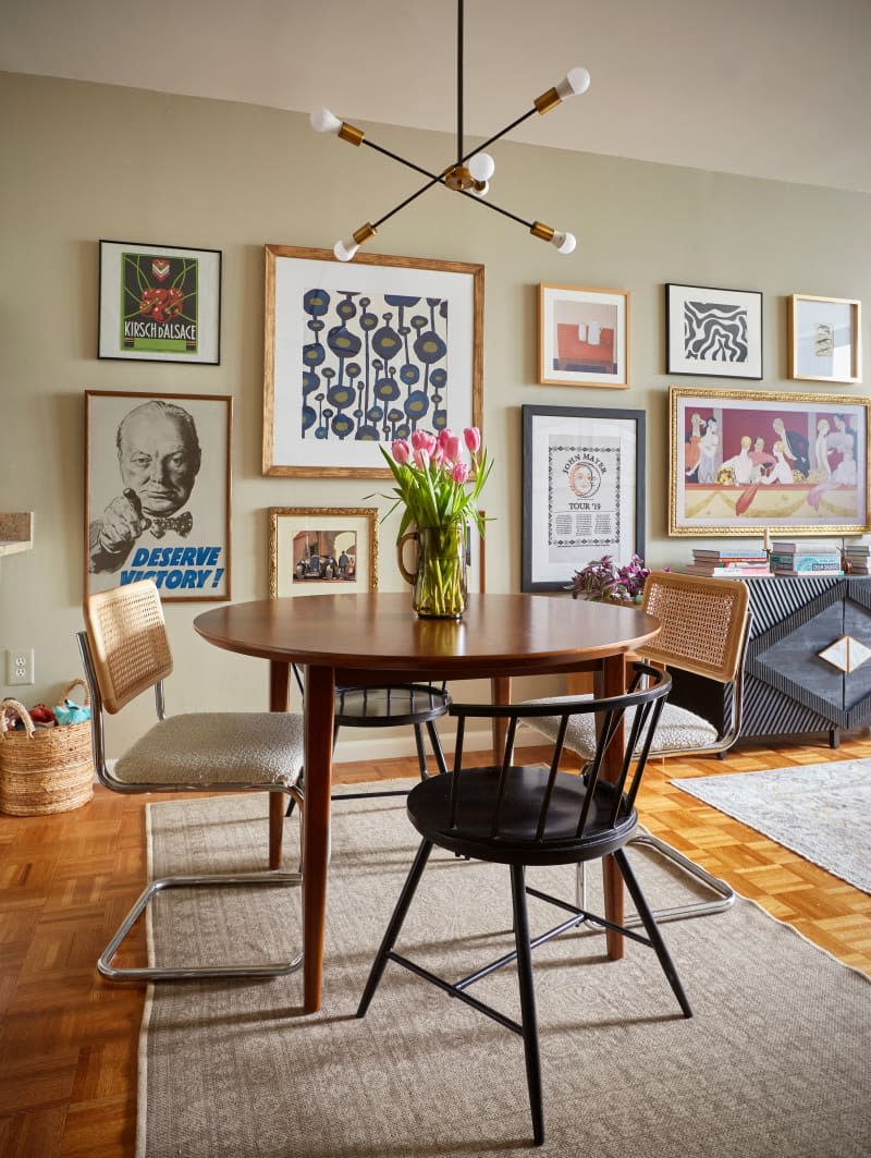 mid century wood round dining table with 2 kinds of dining chairs. vase of tulips on table, gallery wall in back