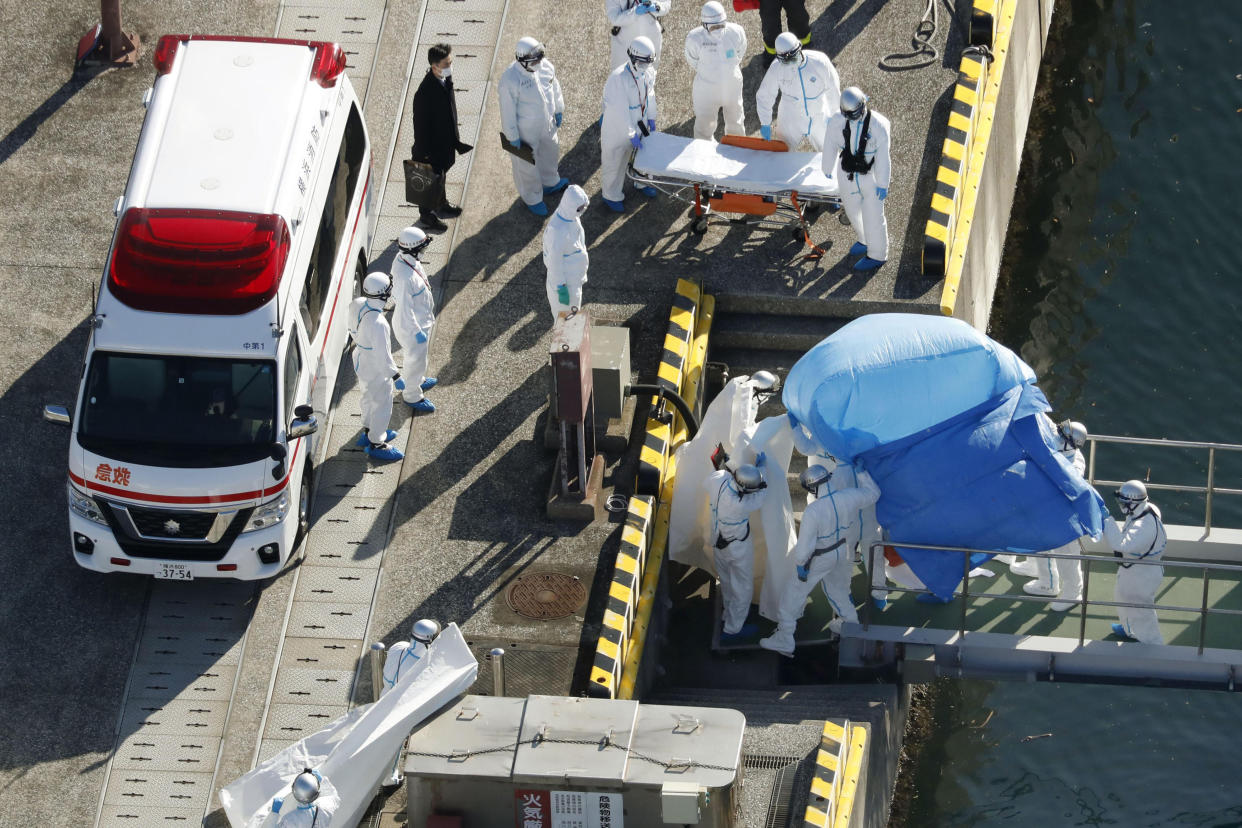 Medical workers in protective suits lead a passenger tested positive for a new coronavirus from the cruise ship Diamond Princess at Yokohama Port in Yokohama, south of Tokyo, Wednesday, Feb. 5, 2020. Japan said Wednesday 10 people on the cruise ship have tested positive for the new virus and were being taken to hospitals. Health Minister Nobukatsu Kato said all the 3,700 people and passengers on the ship will be quarantined on board for up to 14 days under Japanese law. (Hiroko Harima/Kyodo News via AP)