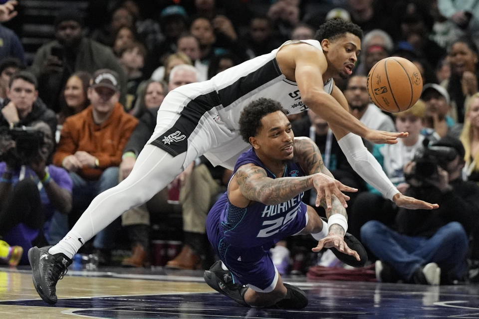 Charlotte Hornets forward P.J. Washington passes under San Antonio Spurs forward Keldon Johnson during the second half of an NBA basketball game on Friday, Jan. 19, 2024, in Charlotte, N.C. (AP Photo/Chris Carlson)