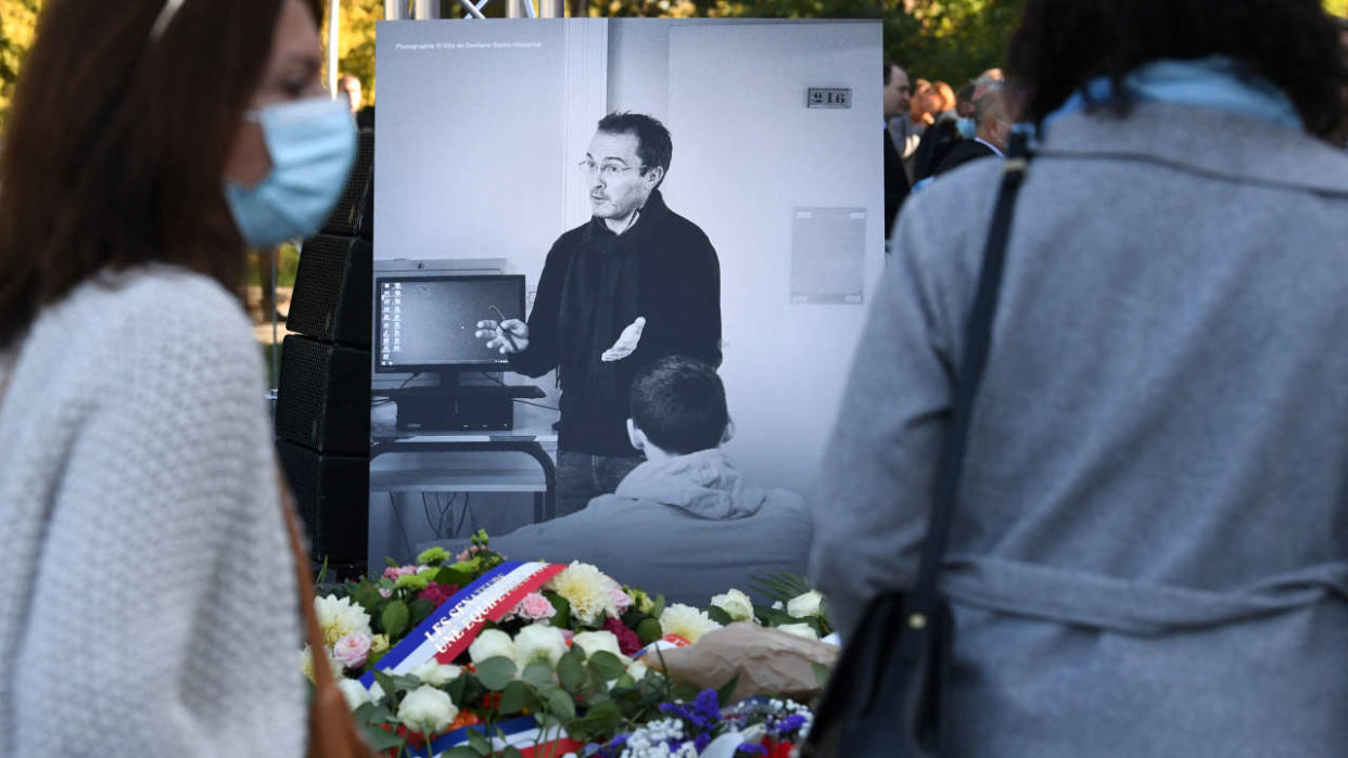 (FILES) In this file photo taken on October 16, 2021, members of the public stand in front of a photograph depicting French history and geography teacher Samuel Paty as they attend a tribute ceremony in Eragny-sur-Oise, northwestern Paris, held one year after Paty was beheaded by an extremist after showing his class cartoons of the Muslim Prophet Mohammed. - The anti-terrorist judges in charge of the investigation into the murder of Samuel Paty in October 2020 in France have closed their investigations on October 6, 2022, AFP learned from a judicial source, confirming a source close to the case. (Photo by Alain JOCARD / AFP)