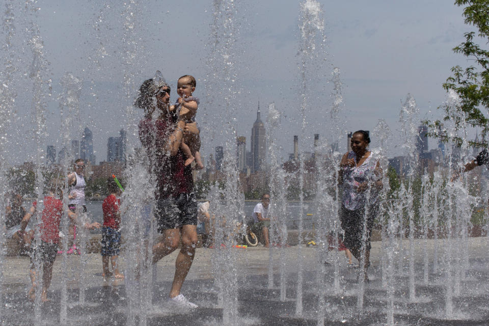 People enjoy the day playing in a water fountain as the Empire State Building is seen from Williamsburg section of Brooklyn on Saturday, July 20, 2019 in New York. Americans from Texas to Maine sweated out a steamy Saturday as a heat wave spurred cancelations of events from festivals to horse races and the nation’s biggest city ordered steps to save power to stave off potential problems. (AP Photo/Eduardo Munoz Alvarez)