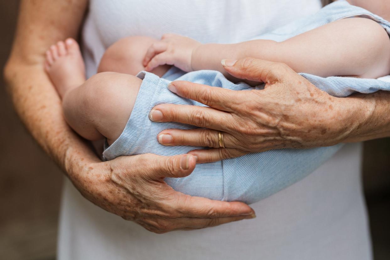an older womans hands holding a new born baby