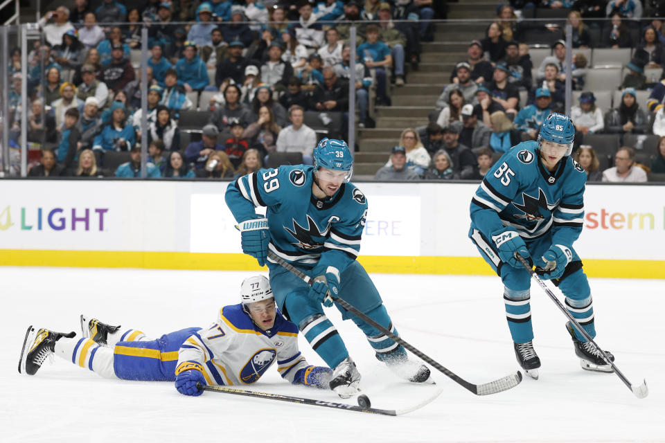 Buffalo Sabres right wing JJ Peterka (77), left, battles for the puck against San Jose Sharks center Logan Couture (39) and defenseman Shakir Mukhamadullin (85) during the second period of an NHL hockey game Saturday, Jan. 27, 2024, in San Jose, Calif. (AP Photo/Josie Lepe)