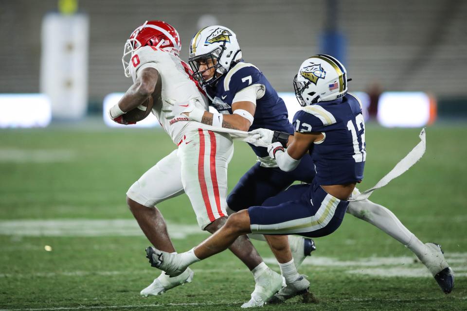 PASADENA, CALIFORNIA - NOVEMBER 25: Peyton Woodyard #7 and Jshawn Frausto-Ramos #12 of the St. John Bosco Braves tackle Jordon Davison #0 of the Mater Dei Monarchs during the 2022 CIF-SS-Ford Division 1 Football Championship at Rose Bowl Stadium on November 25, 2022 in Pasadena, California. (Photo by Meg Oliphant/Getty Images)