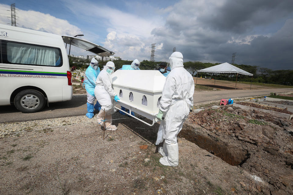 Workers wearing personal protective equipment (PPE) carry the body of a Covid-19 victim at a cemetery in Shah Alam February 11, 2021. — Picture by Yusof Mat Isa