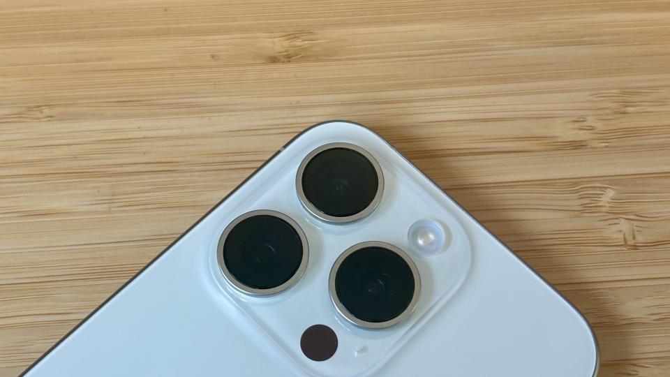 A grey titanium iPhone 15 Pro camera phone on a wooden desk