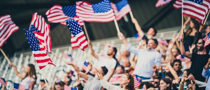 People standing and waving USA flags on a stadium during sport event.