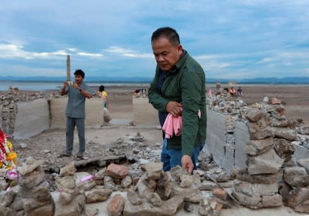 A man prays while another takes pictures at the ruins of a Buddhist temple which has resurfaced in a dried-up dam due to drought, in Lopburi, Thailand
