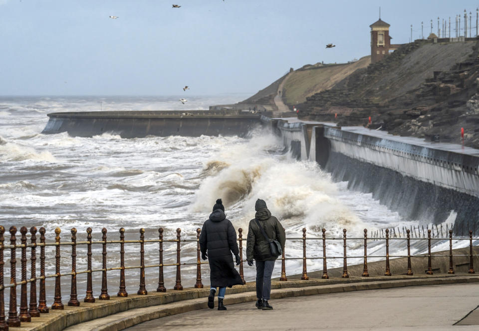 People walk near breaking waves on the sea front in Blackpool, England, Monday, Jan, 22, 2024. The U.K.'s Met Office weather service had issued an unusual blanket wind warning for the whole country before Storm Isha, which reached its peak overnight. A 99-mile-an-hour gust was recorded at Brizlee Wood radar station in northeastern England. (Danny Lawson/PA via AP)