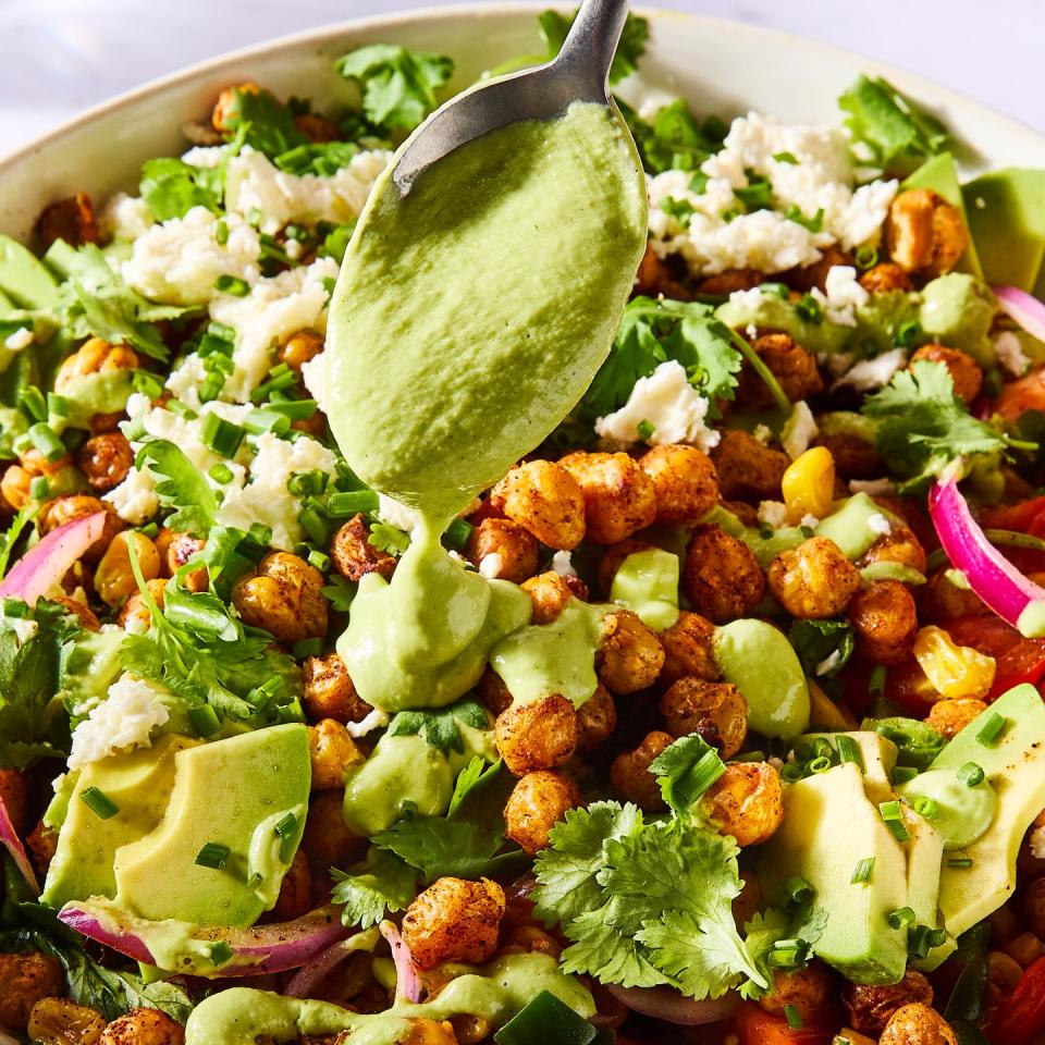 salad tossed with crispy chickpeas, avocado slices, red onions, sliced tomatoes, corn, and topped with herbs and cheese