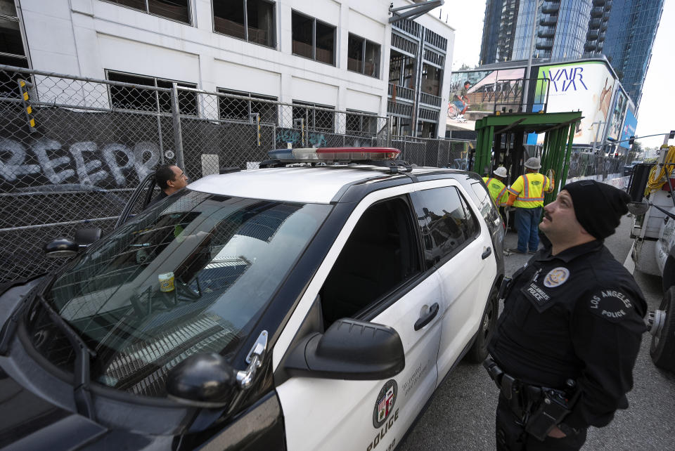 Los Angeles Police officers guard the exterior of an unfinished complex of high-rise towers that have recently been vandalized with graffiti and used for dangerous social media stunts after the developer ran out of money is seen in downtown Los Angeles Friday, Feb. 16, 2024. The three towers have become an embarrassment in a high-profile area that includes Crypto.com Arena, home of major sports teams and events such as the Grammys, as well as the Los Angeles Convention Center and the L.A. Live dining and events complex. (AP Photo/Damian Dovarganes)