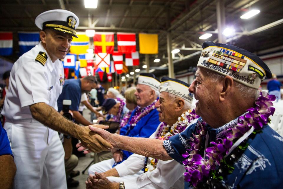 U.S. Navy Captain Mark Manfredi greets U.S.S. Arizona crewmember Lou Conter (right) before the start of a memorial service marking the 74th Anniversary of the attack on the U.S. naval base at Pearl Harbor on December 07, 2015, on the island of Oahu at the Kilo Pier at Joint Base Pearl Harbor-Hickam in Honolulu, Hawaii.