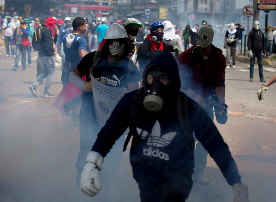 Masked anti-government demonstrators walk amid teargas fired by Bolivarian National Police during a protest to demand the release of arrested student protesters in Caracas, Venezuela, Monday, May 12, 2014. Venezuelan courts have ordered 11 student protesters to stand trial, but they have freed more than 150 others arrested with them during raids on encampments set up by protesters opposed to President Nicolas Maduro's government. (AP Photo/Fernando Llano)