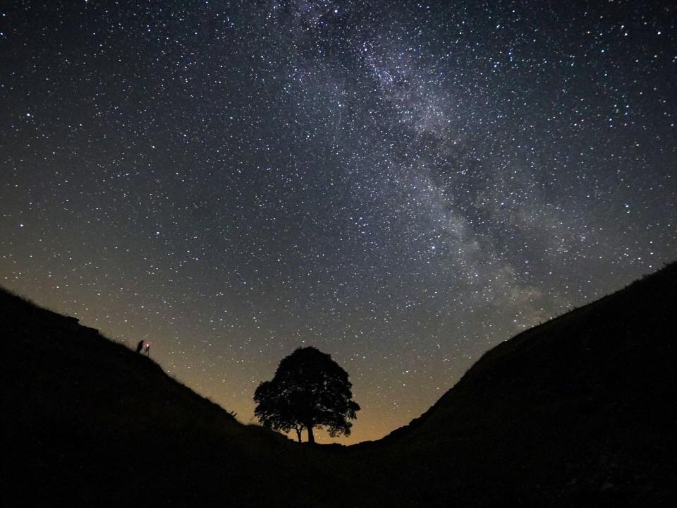 A photographer lining up a shot on a clear night under the Milky Way at Sycamore Gap on Hadrian’s Wall in Northumberland (Owen Humphreys/PA)