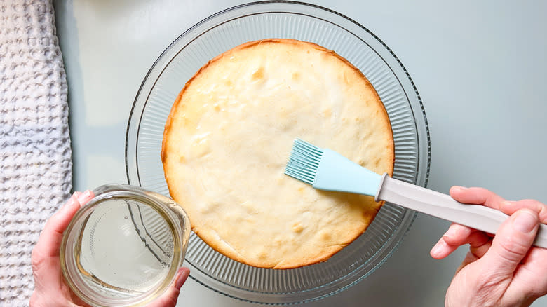 Brushing lavender simple syrup on bright and sunny lemon lavender cake layer on serving platter with pastry brush