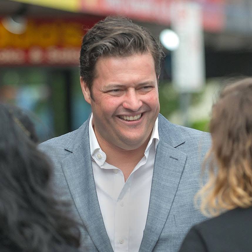 Pictured is Burwood MP Will Fowles smiling white speaking to people. 