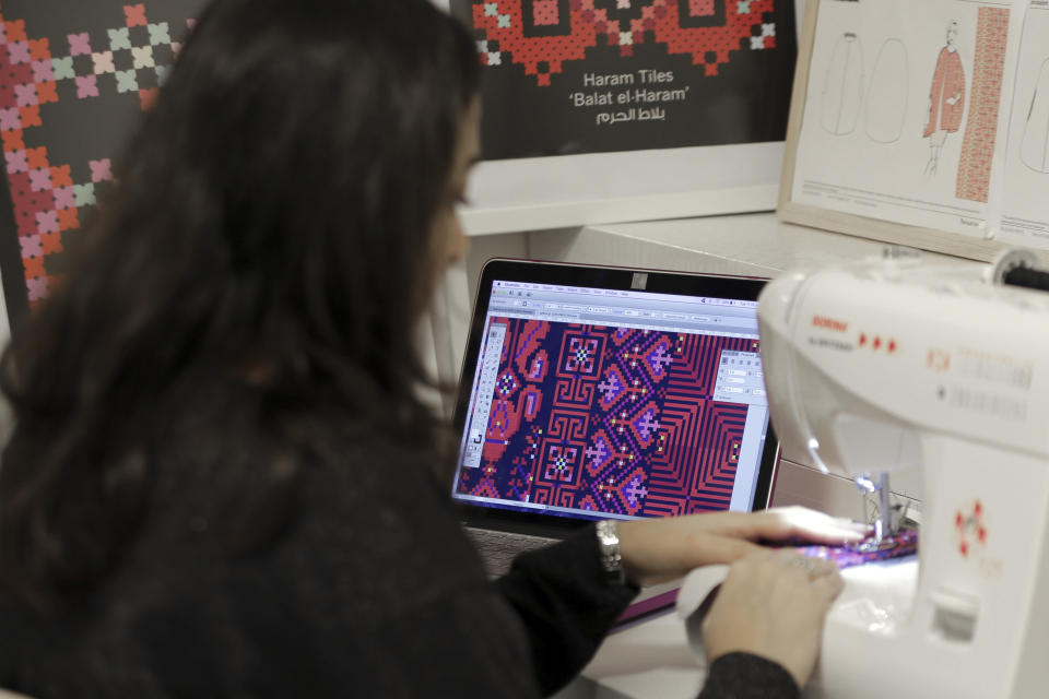 In this Tuesday, Jan. 29, 2019 photo, designer Natalie Tahhan works in her studio in east Jerusalem. The thobe, a brightly embroidered robe for women, has long been a staple of Palestinian life, sewn by village women and worn at weddings and parties. Tahhan produces capes from digital prints that replicate traditional embroidery stitches, “connecting tradition with what is new and stylish.” (AP Photo/Mahmoud Illean)