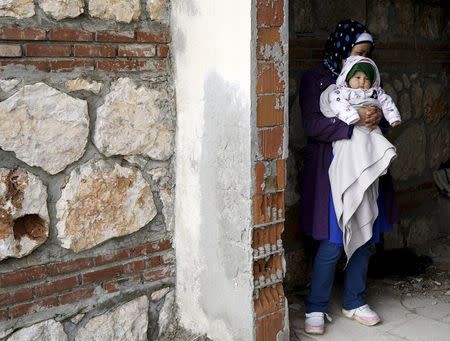 An Afghan refugee woman stands with her baby at the entrance of an old abandoned beach house as they wait to board a dinghy sailing off for the Greek island of Chios, while they try to travel from the western Turkish coastal town of Cesme, in Izmir province, Turkey, March 6, 2016. REUTERS/Umit Bektas