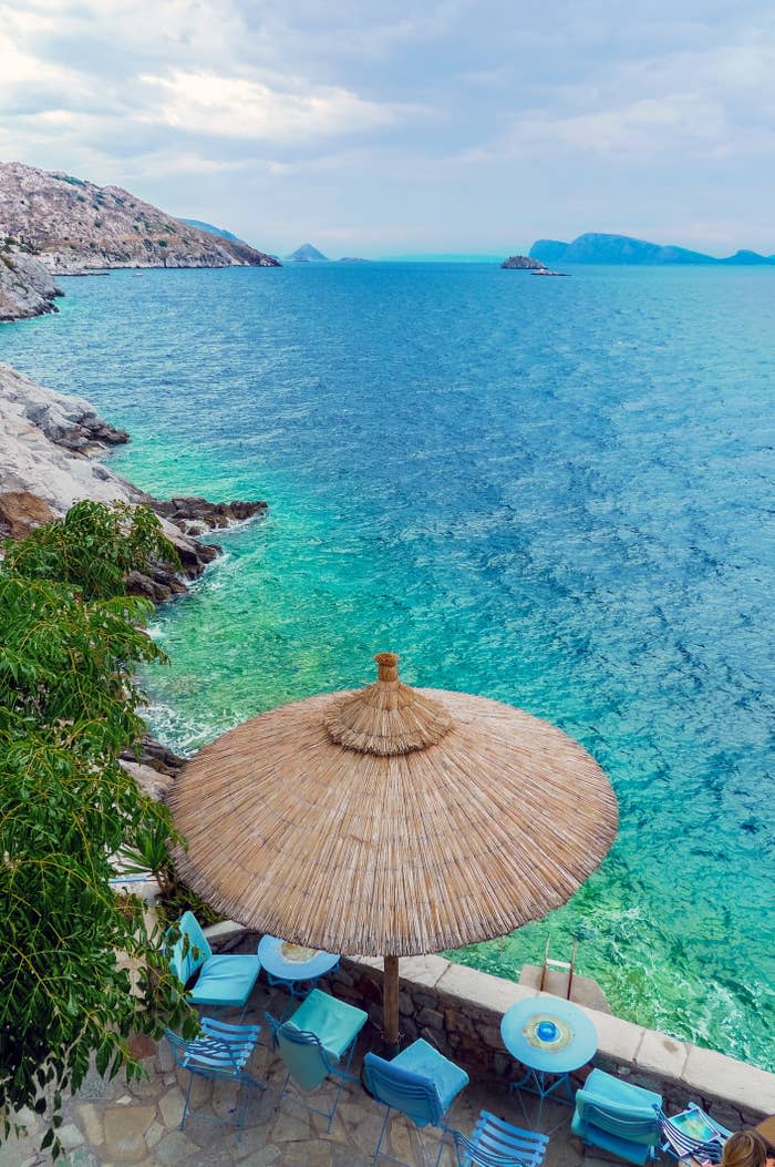 Seaside cafe with straw umbrella and chairs overlooking clear blue water