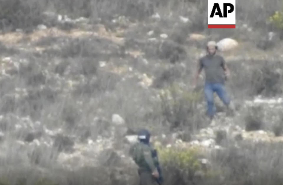 In this image made from video, a settler, right, speaks with an Israeli security guard near Burin, West Bank, Friday, Oct. 21, 2022. An Israeli rights group has released a video that appears to show an Israeli security guard and a Jewish settler joining forces during a clash with Palestinian farmers in the occupied West Bank, with the settler throwing a stun grenade after the guard apparently shows him where to aim. (AP Photo)