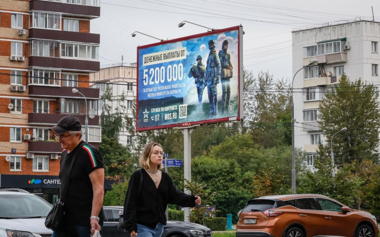 People walk near a banner with an advertising poster calling for military conscription in Moscow