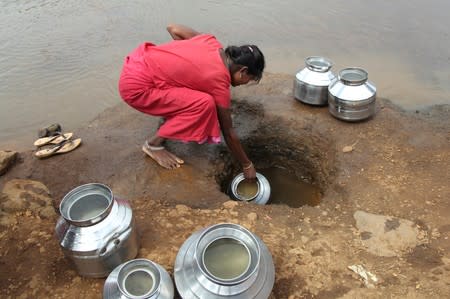 A woman fetches water from an opening made to filter water next to a polluted lake in Thane