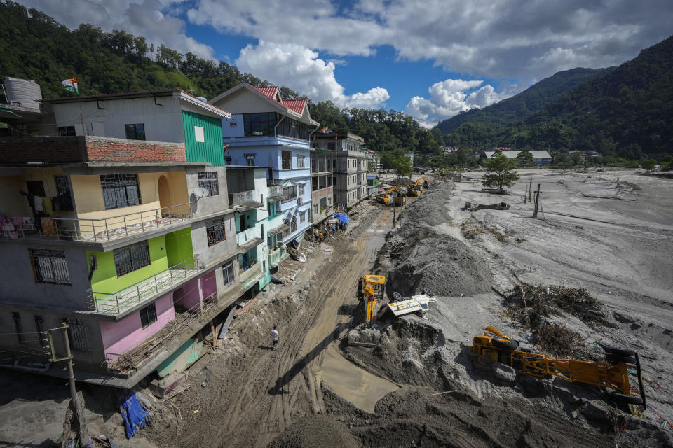 Vehicles that got washed away in floods lie on the sand as machinery is used to clean mud and sand near the buildings along the Teesta river in Rongpo, east Sikkim, India, Sunday, Oct. 8. 2023. Rescuers continued to dig through slushy debris and ice-cold water in a hunt for survivors after a glacial lake burst through a dam in India’s Himalayan northeast, shortly after midnight Wednesday, washing away houses and bridges and forcing thousands to flee. (AP Photo/Anupam Nath)