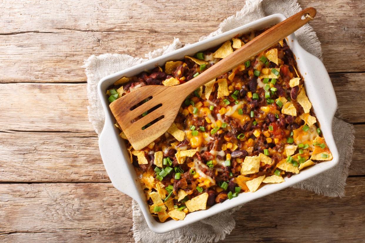 Frito casserole in white baking dish with a wooden spatula on a rustic wooden table