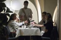 A waiter wearing a face mask and gloves to protect against coronavirus, serve customers in a restaurant at Patriarshiye Prudy, a hip restaurant and bar district in Moscow, Russia, late Friday, Oct. 16, 2020. The outbreak in Russia this month is breaking the records set in the spring, when a lockdown to slow the spread was put in place. But, as governments across Europe move to reimpose restrictions to counter rising cases, authorities in Russia are resisting shutting down businesses again. (AP Photo/Pavel Golovkin)