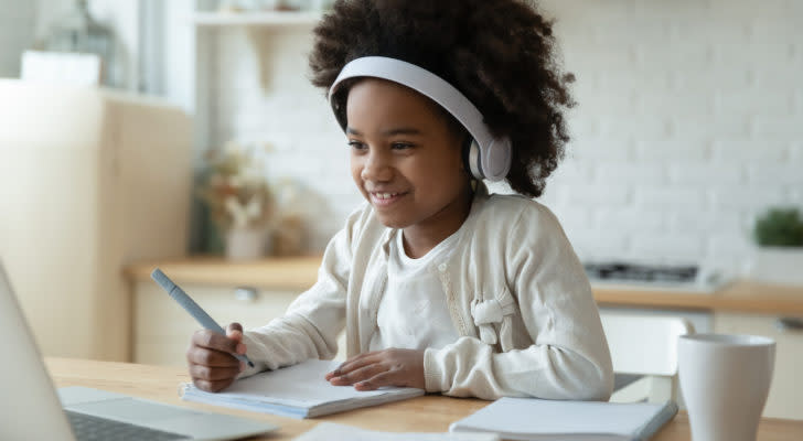 a girl sitting in front of a laptop working on homework. investing for kids