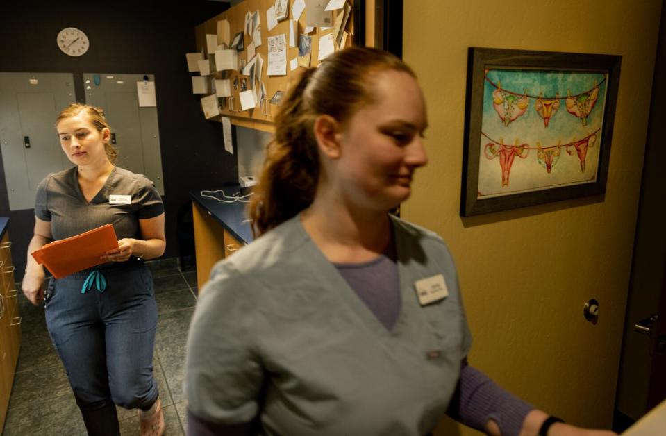 Nurses carry charts to exam rooms past thank you cards tacked to cupboards and artwork of a uterus hanging on a clothesline.