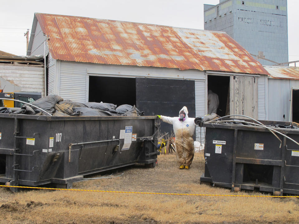 In this photo taken on Wednesday, April 23, 2014, white-suited workers wearing respirators clean up the illegal filter sock dump in an abandoned gas station in Noonan, N.D., near the Canadian border. Radiological readings were to be conducted to be sure the building and soil was back to normal. (AP Photo/The Bismarck Tribune, Lauren Donovan)