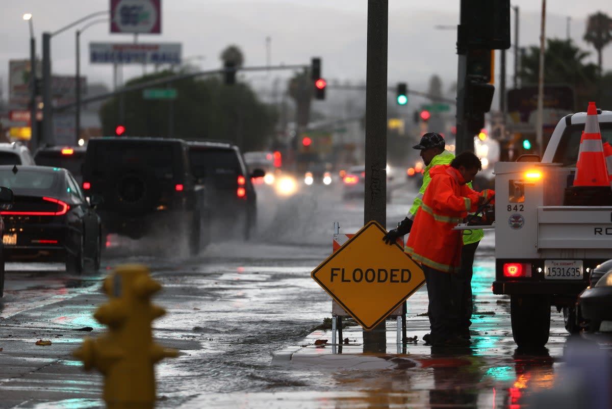 Workers set up a sign near a flooded intersection as tropical storm Hilary moves through California (Getty Images)