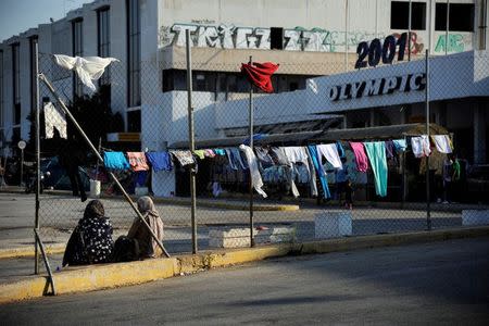 Two women sit by a wire fence with laundry hanging on it, outside the disused Hellenikon airport, where stranded refugees and migrants are temporarily accommodated in Athens, Greece, August 10, 2016. REUTERS/Michalis Karagiannis