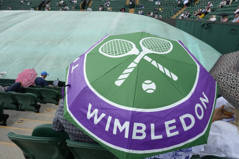 FILE - Spectators sit under an umbrella on a covered court after rain delayed the start of play on day three of the Wimbledon tennis championships in London, Wednesday, July 5, 2023. This year's Wimbledon tournament begins on Monday, July 1.(AP Photo/Kirsty Wigglesworth, File)