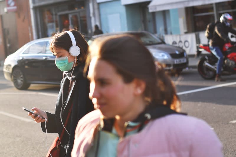 Pedestrians cross the road as a woman wears a protective mask in London