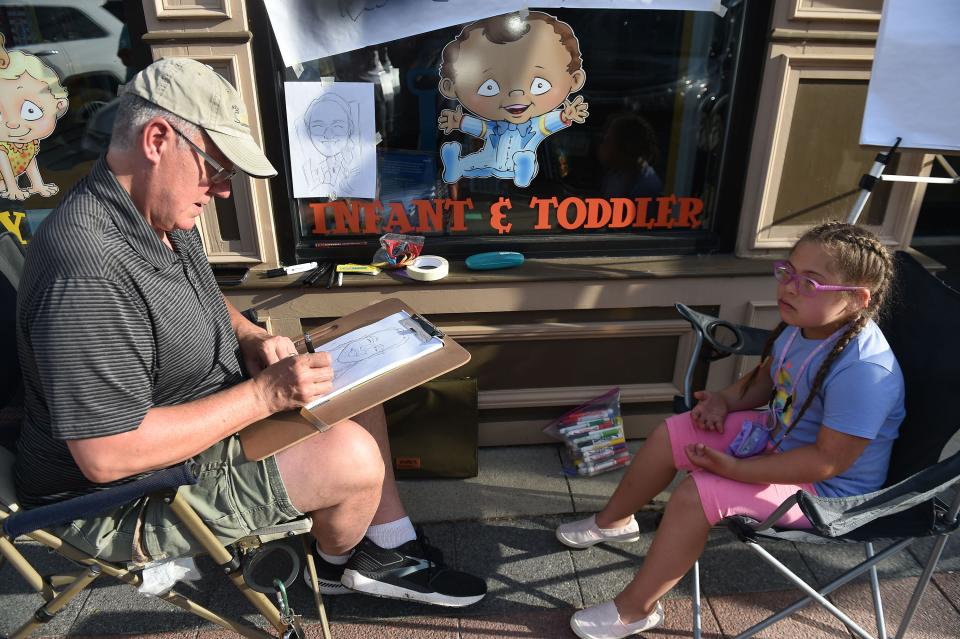 Seven-year-old Zayah Jackson poses for a portrait as artist Tim Read makes a caricature during the Art Walk in 2021. Read will return to the Art Walk Thursday and can be located at Duck Worth Wearing.