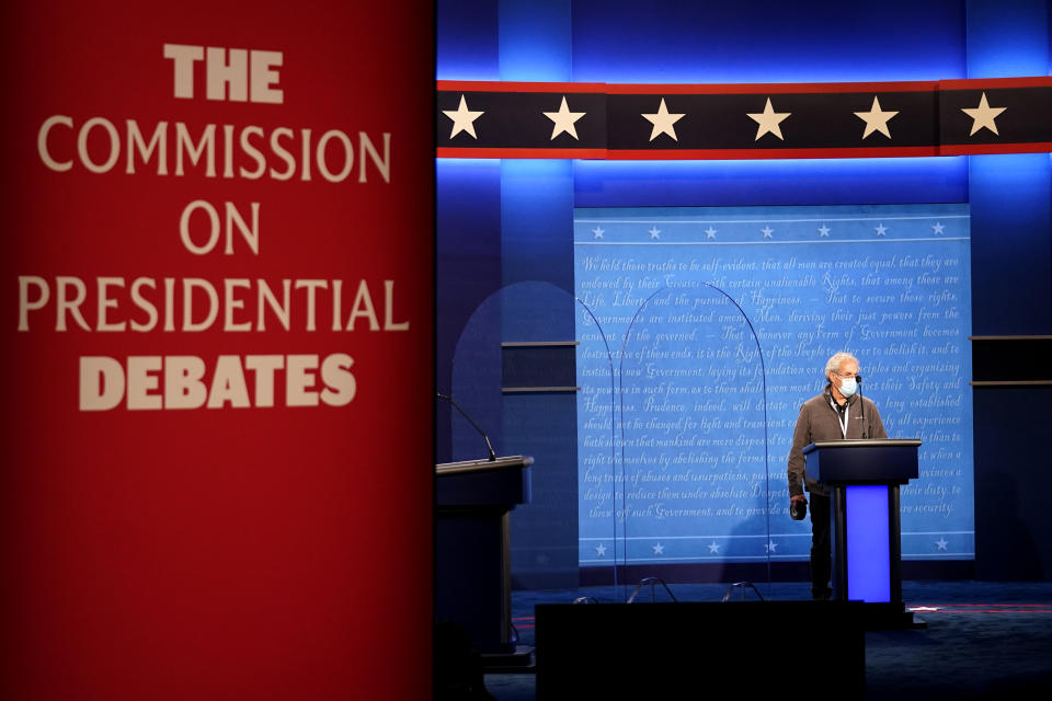 A member of the production crew stands at a podium near glass barriers to prevent the spread of COVID-19 on stage ahead of the final presidential debate between Republican candidate President Donald Trump and Democratic candidate former Vice President Joe Biden, Wednesday, Oct. 21, 2020, in Nashville, Tenn. The debate will take place Thursday, Oct. 22 at the Curb Event Center at Belmont University. (AP Photo/Julio Cortez)