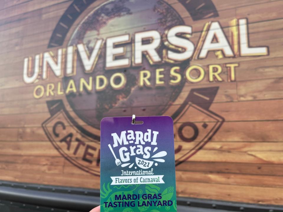 hand holding a mardi gras pass in front of a universal studios orlando sign