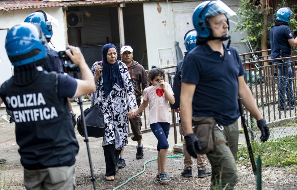 Police escort people from an abandoned school which they had occupied on the outskirts of Rome, Monday, July 15, 2019. Police are evicting migrants and Italians from an abandoned former school on Rome's outskirts in the latest operation to empty occupied buildings of migrants and squatters. (Massimo Percossi/ANSA via AP)