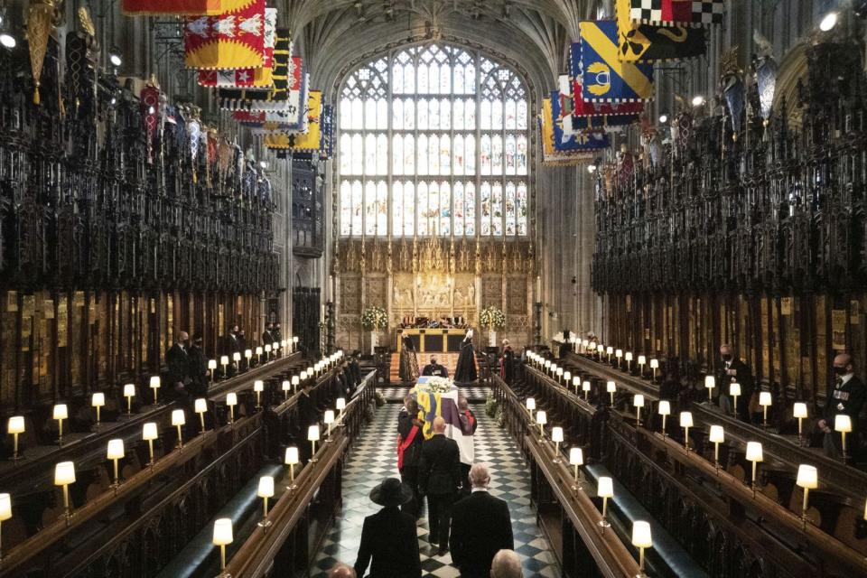 The coffin is carried by pallbearers followed by mourners in St. George's Chapel past pews with a few people in them.