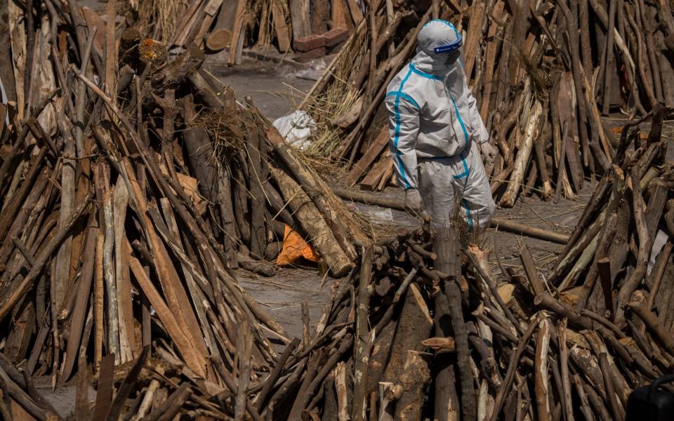 A man wearing PPE walks between funeral pyres before a mass cremation - Anindito Mukherjee/Getty Images